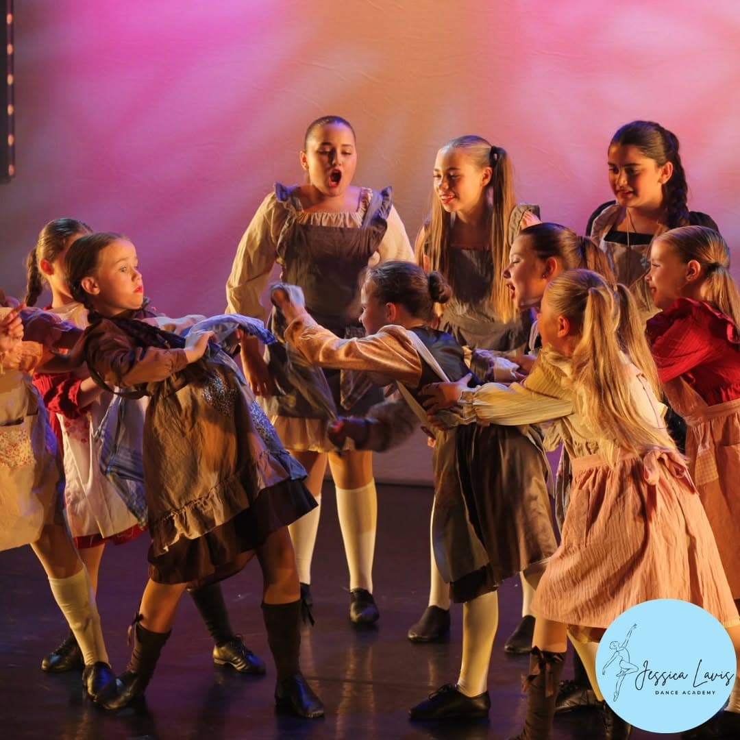 A cast of young dancers in costume acting out a theatrical scene on stage