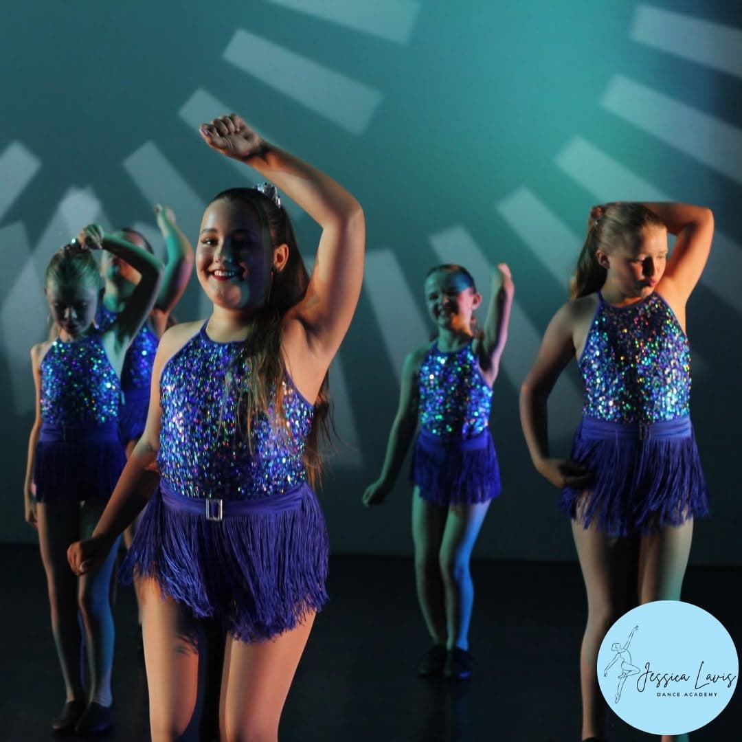 A line of dancers in blue sequin costumes striking a pose on stage