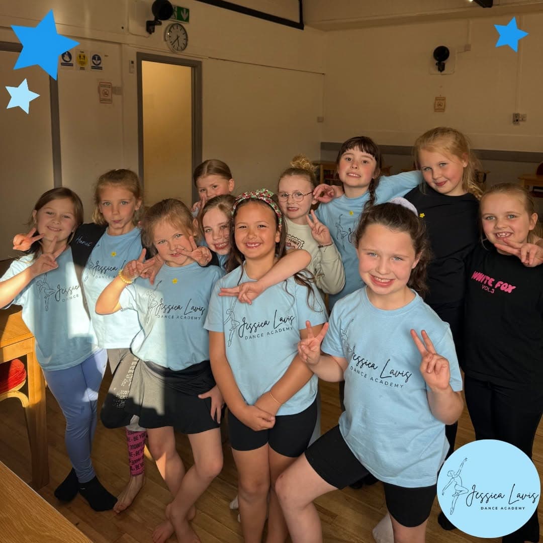 A big class of dancers grinning with peace signs in a sunlit hall