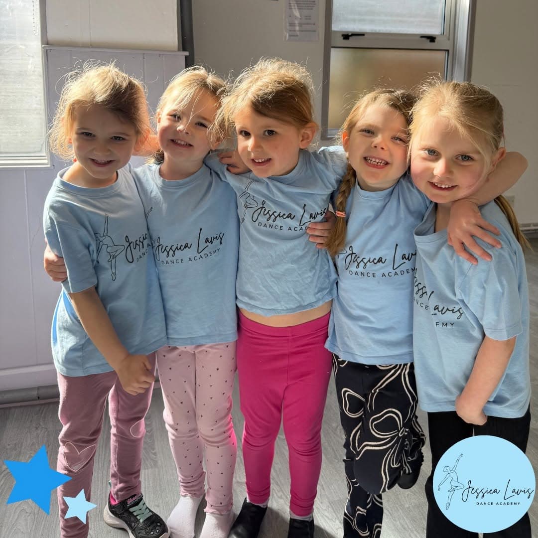 Five mini dancers in light blue JLDA t-shirts sharing a group hug in the studio