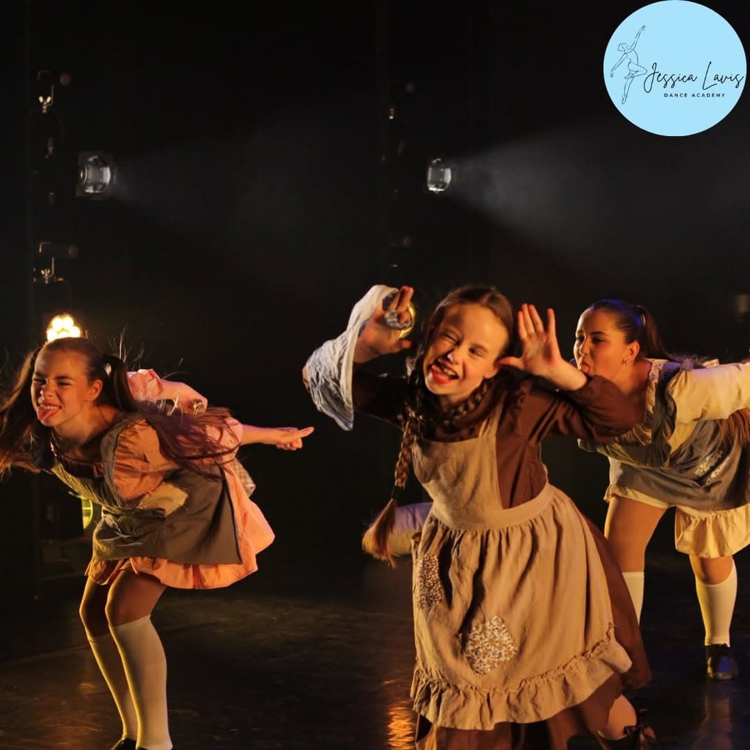 Three dancers in vintage pinafore costumes pulling cheeky faces mid-routine