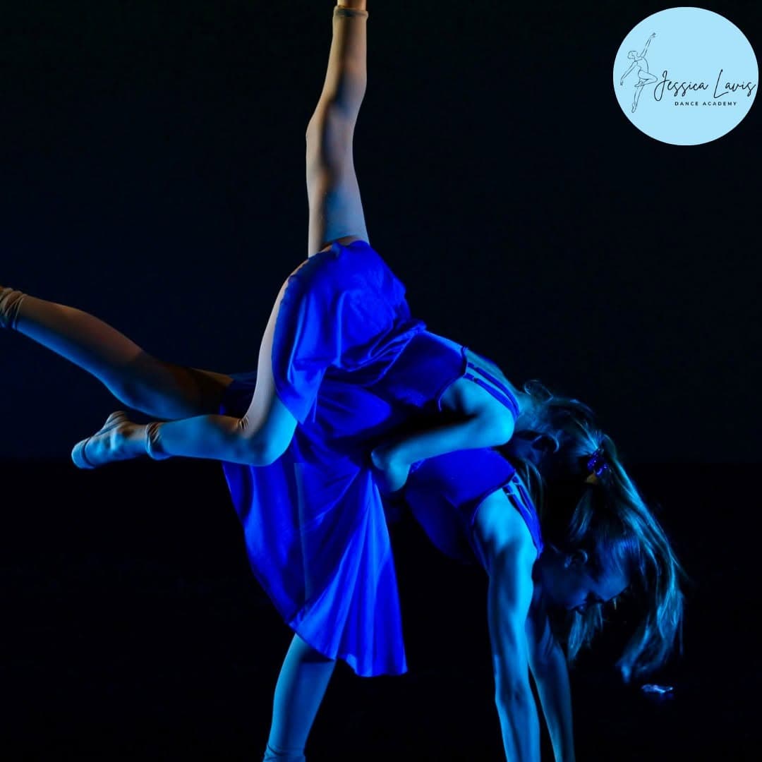 Two dancers in blue lyrical dresses performing a lift on a darkened stage