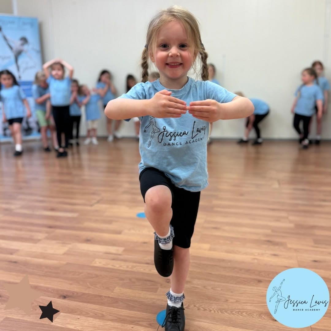 A young dancer in tap shoes balancing on one leg in class